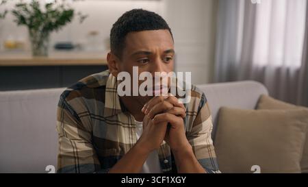 Pensive serious African American man at couch considering problem solution solving difficult trouble thoughtful hesitate male guy thinking rubbing Stock Photo