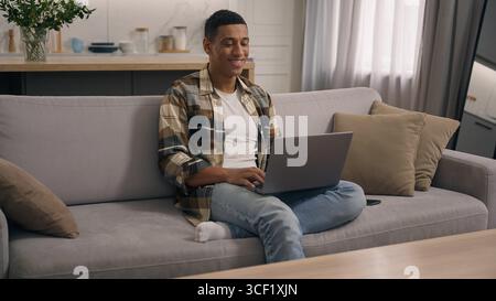 Happy African American man at home using computer app shopping e-commerce at couch apartment male guy freelancer working laptop indoors student e Stock Photo