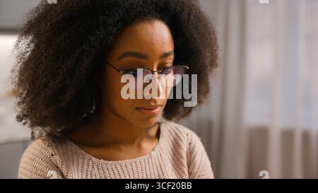 Serious concentrated African American woman female girl putting on glasses eyeglasses businesswoman starting working at home open laptop looking at Stock Photo