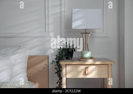 Bedside table with lamp and other decor near bed indoors Stock Photo
