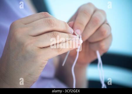 Close-up of hands threading a needle with white thread, preparing for sewing or tailoring Stock Photo