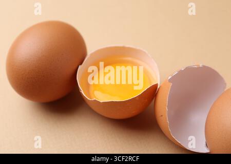 Whole and broken chicken eggs on beige background, closeup Stock Photo