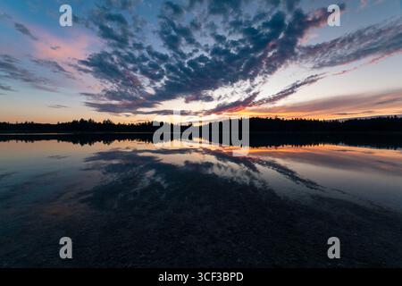 The colourful glowing sky at dusk is reflected in calm waters of Lake Fohnsee in summer, Osterseen Nature Reserve, Bavaria, Germany Stock Photo