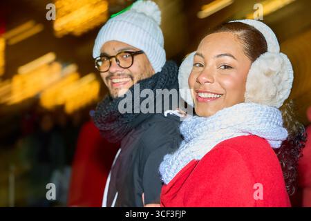 Young latin couple wearing winter clothes smiling and having fun together during christmas holidays at a night street market Stock Photo