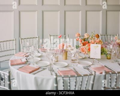 A beautifully arranged dining table with flowers, glassware, and table settings ready for guests in a modern interior. Stock Photo
