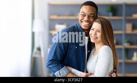Portrait Of Young Loving Multiracial Couple Embracing At Home Stock Photo