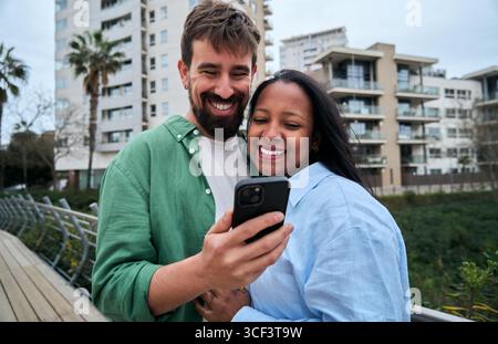 Happy multiracial couple using smartphone outdoors in the city Stock Photo