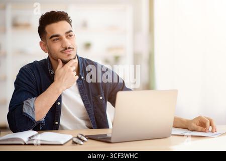 Dreamy young man sitting at office, looking at copy space Stock Photo