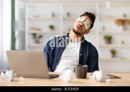 Tired arab guy with eyes drawing sleeping at workdesk Stock Photo
