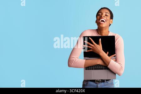 Online Shopping Lover. Cheerful Black Lady Embracing Opened Laptop And Laughing Stock Photo