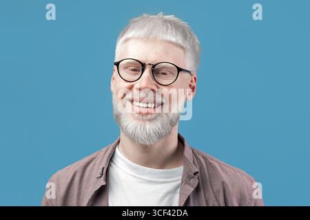 Headshot portrait of happy man with pale skin wearing eyeglasses, looking and smiling at camera on turquoise background Stock Photo
