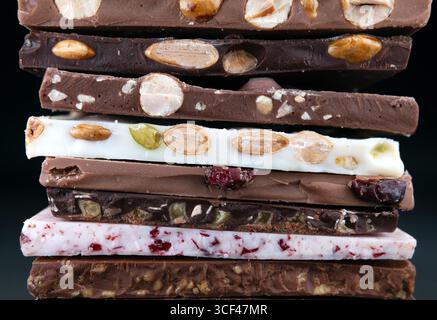 Handcrafted Belgian chocolate bars with nuts and dried fruits, stacked in a colorful and textured arrangement. Stock Photo