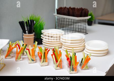 A selection of fresh vegetable appetizers arranged in individual cups with dips. plates and utensils are neatly set on a table, ready for a gathering Stock Photo