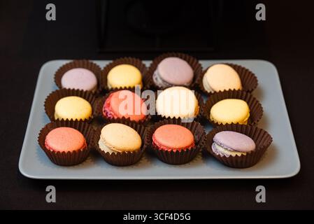 A variety of colorful macarons are neatly arranged on a rectangular tray. each sweet treat sits in a paper cup, showcasing vibrant pastel hues and tem Stock Photo