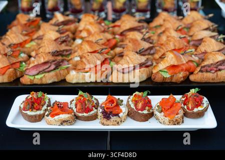 A mouthwatering assortment of appetizers and sandwiches featuring croissants with various fillings and artisanal open-faced bites, ideal for events an Stock Photo