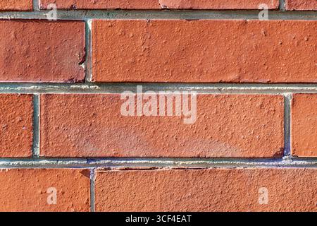 A closeup view of a red brick wall with sharp geometry and industrial precision. Subtle imperfections, chipped edges, and faint blue discolorations. Stock Photo