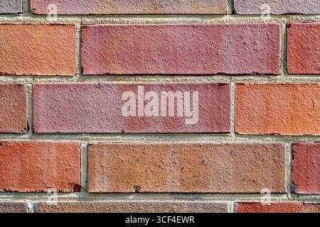 A closeup of a textured brick wall with variations in red, brown, and orange tones and a stained surface. Stock Photo