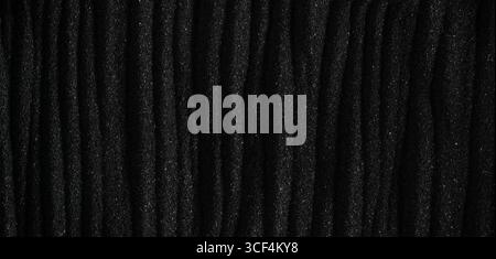 Dark black sand. Stripes and ripples of smooth volcanic sand texture or wallpaper. Wave pattern in black sand background. Stock Photo