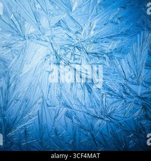 Snowflake frost patterns on glass. Vivid ice crystal textures on clear glass window. Frozen surface, snow flake structure, or freezing cold winter bac Stock Photo