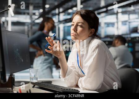 Pensive server hub engineer looking at data visualization on PC, thinking how to fix performance issues. Data center worker looks at analysis graph, brainstorming how to repair hardware failures Stock Photo