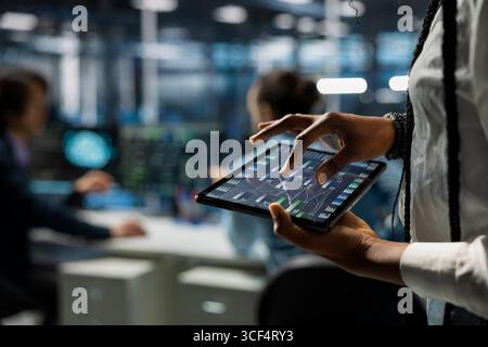 Close up of data center programmer monitoring AI systems using tablet, adjusting machine learning parameters. Server farm worker enhancing artificial intelligence technology performance with device Stock Photo