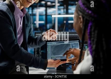 Close up of programmers coding on tablet in data center, updating AI driven automation scripts. IT workers using device in server room, programming artificial intelligence algorithms, debugging gear Stock Photo
