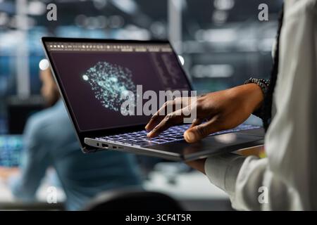 Close up of IT professional in data center using AI LLM assistant on laptop to do maintenance on equipment rigs. Server hub computer scientist using large language model chatbot to do backups Stock Photo