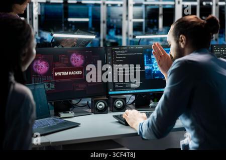Technicians in AI server farm doing brainstorming to fix hacking incident involving theft of sensitive data. Data center coworkers working together to stop computer virus triggered by security systems Stock Photo