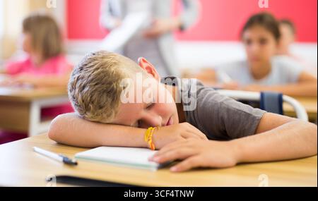 Tired school boy sleeping in classroom during lesson Stock Photo