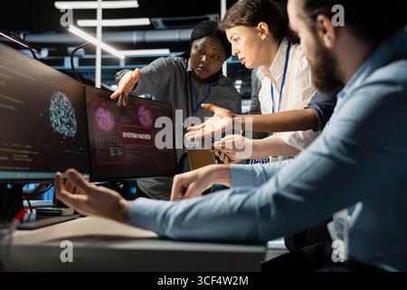 Programmers in AI data center reacting to virus alert, initiating protocol to protect critical systems. Server room IT experts doing brainstorming, assessing compromised gear after hacker attack Stock Photo