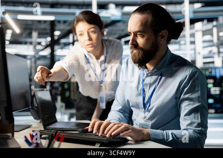 Programmers in data center workplace using computer, verifying firewall configurations. Teamworking colleagues doing brainstorming, performing equipment vulnerability scans in server hub using PC Stock Photo