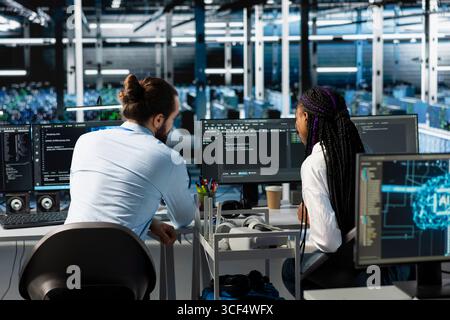 Manager and intern in server room using PC to review infrastructure diagnostics. IT specialist and trainee in data center analyzing performance data to maintain system uptime Stock Photo
