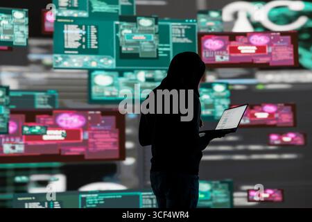 Young guy hacker breaking into a system in stealth mode by programming code, bypassing firewalls and exploiting vulnerabilities in network security to carry out cyber attack and infiltration. Stock Photo