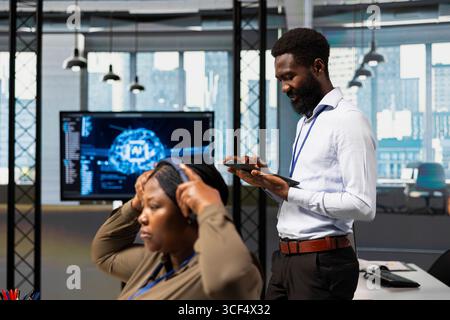 Computer scientist utilizing artificial intelligence to optimize performance using tablet. African american engineer in office training machine learning models with device Stock Photo