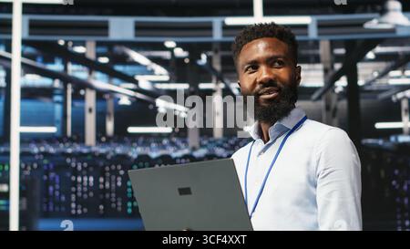 Portrait of cheerful data center engineer analyzing gear issues using node tree tools. Upbeat African american server hub specialist using AI visualization insights to optimize system health, camera B Stock Photo
