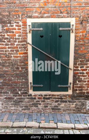Frontal view of an old window with locked shutters in a weathered brick wall. Stock Photo
