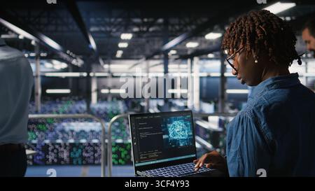 System administrators in data center monitoring AI LLM visualization. African american server farm coworkers overseeing rigs powering machine learning processes, Stock Photo