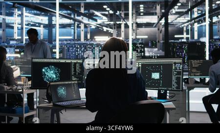 Data center programmer entering office uses node tree program to identify equipment performance issues. Server hub worker sitting at desk, reviewing data analysis graph to minimize failures, camera A Stock Photo