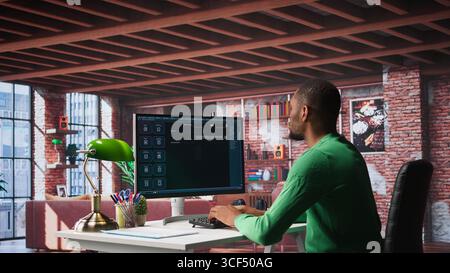 Black male freelancer at home uses AI chatbot for task completion, automation and machine learning. Young adult uses artificial intelligence to generate new ideas with prompts. Camera B. Stock Photo