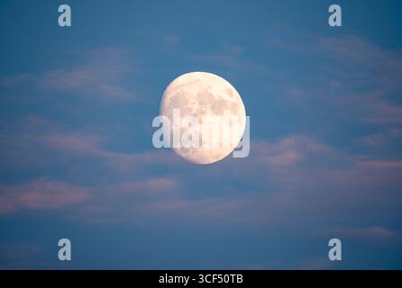 Almost full moon in the sky during sunset with pink clouds surrounding it. Stock Photo