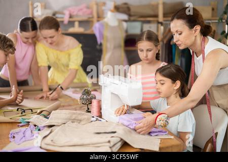 Teacher encouraging preteen girl during sewing lesson for kids Stock Photo