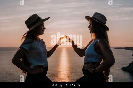 Silhouettes of Two Women Making Heart Shape at Sunset Stock Photo
