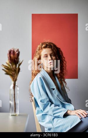 Vertical studio portrait of attractive young Caucasian woman with long curly red hair looking at camera Stock Photo