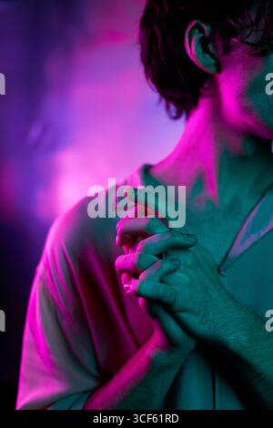 Vertical medium close-up shot of unrecognizable young man standing with hands folded in blue and pink neon light Stock Photo