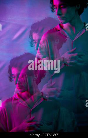 Vertical medium multiple exposure studio portrait shot of handsome young Caucasian man standing with hands on chest in neon light Stock Photo