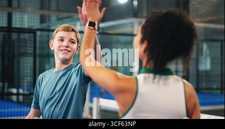 Happy boy, teenager and high five with coach for padel tennis match, winning or indoor sport. Junior player, trainer and touch with smile in court for Stock Photo