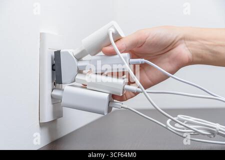 Hand inserting electrical plugs into outlet. Electrical overload Stock Photo