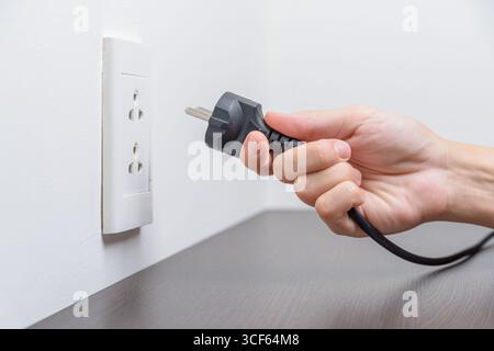 Female hand inserting a black electrical plug into outlet Stock Photo
