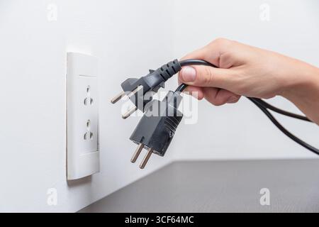 Hand inserting electrical plugs into outlet. Electrical overload Stock Photo