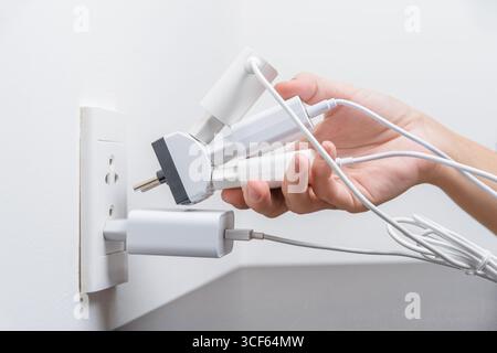 Hand inserting electrical plugs into outlet. Electrical overload Stock Photo